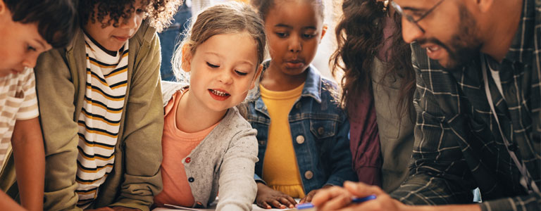 School kids crowded around a table of coloring books with teacher